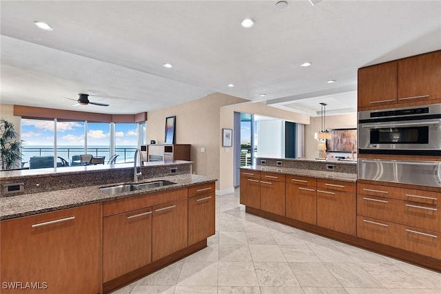 kitchen with decorative light fixtures, sink, oven, dark stone counters, and a water view