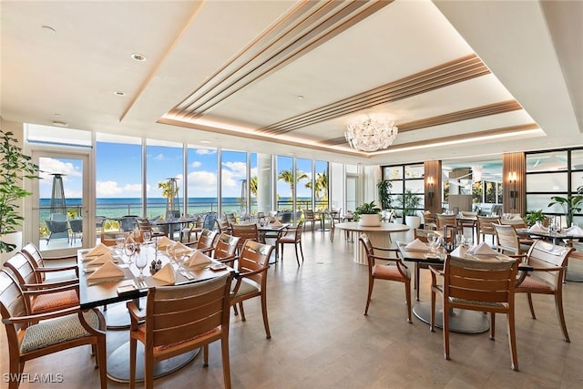 dining room with a water view, floor to ceiling windows, a tray ceiling, and a notable chandelier