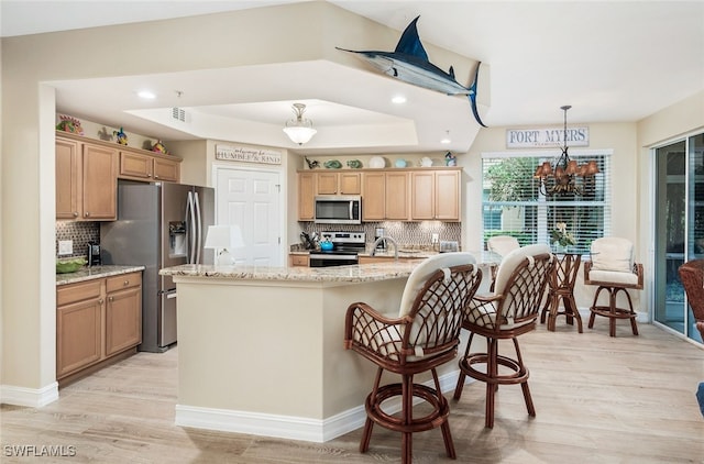 kitchen with pendant lighting, a kitchen island with sink, stainless steel appliances, and a raised ceiling