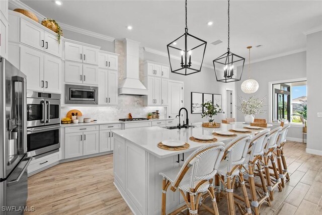 kitchen with pendant lighting, sink, stainless steel appliances, an island with sink, and custom exhaust hood