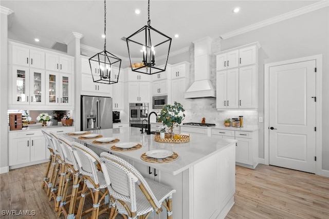 kitchen with a spacious island, light countertops, appliances with stainless steel finishes, light wood finished floors, and custom range hood