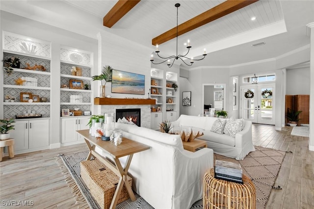 living room featuring built in shelves, beam ceiling, french doors, light wood-style flooring, and a glass covered fireplace