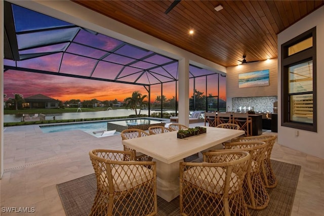 patio terrace at dusk with a water view, a lanai, and pool water feature