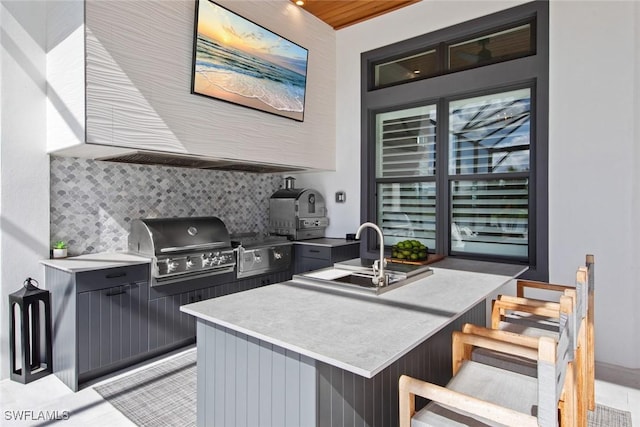 kitchen with tasteful backsplash, a breakfast bar area, gray cabinets, light countertops, and a sink