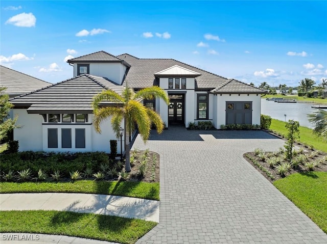 view of front of house with decorative driveway, french doors, stucco siding, a water view, and a tiled roof