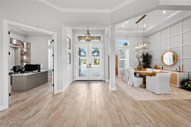 entrance foyer with a towering ceiling, ornamental molding, light hardwood / wood-style floors, an inviting chandelier, and french doors