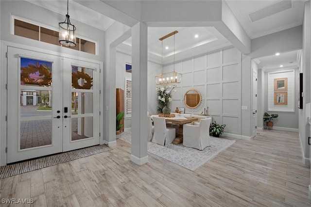 entrance foyer with wood finished floors, crown molding, french doors, a decorative wall, and a notable chandelier