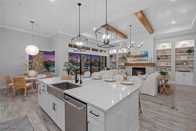 kitchen with sink, white cabinetry, decorative light fixtures, stainless steel dishwasher, and an island with sink