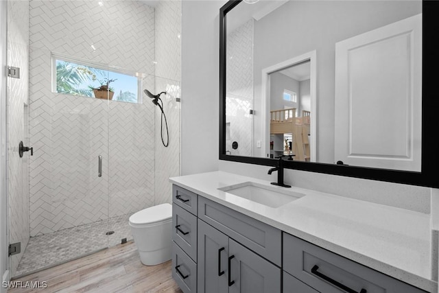 bathroom featuring wood finished floors, a shower stall, toilet, and vanity