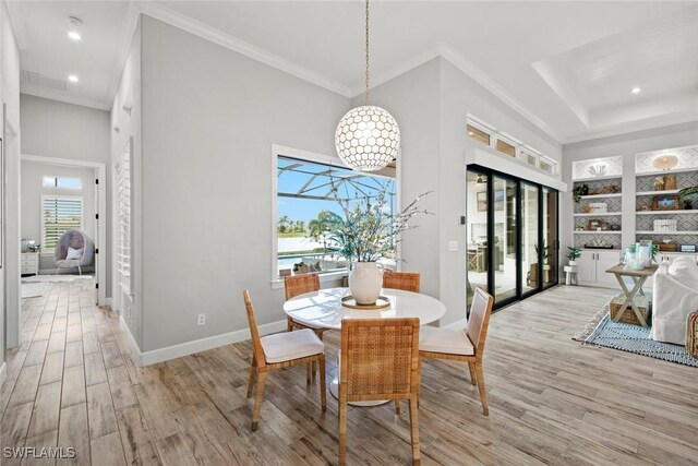 dining space with crown molding, a towering ceiling, built in features, and light wood-type flooring