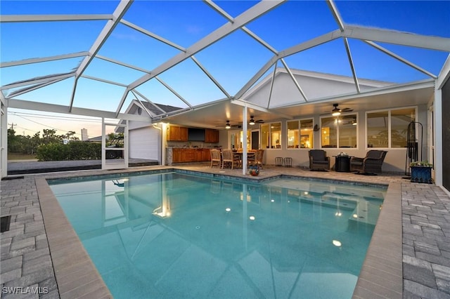 pool at dusk featuring a bar, outdoor lounge area, a lanai, ceiling fan, and a patio area