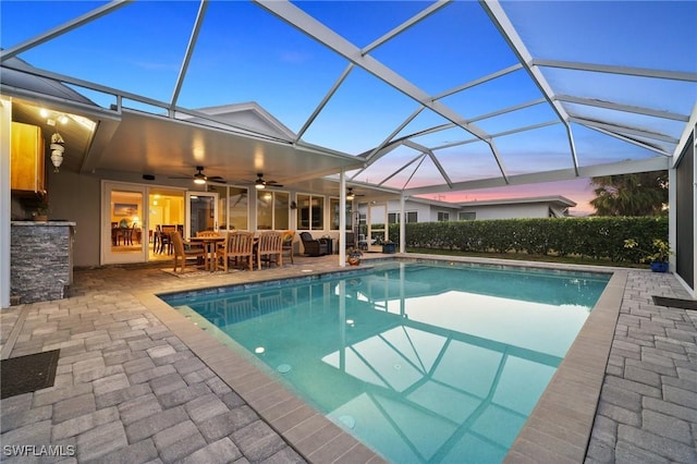 pool at dusk featuring a lanai, a patio area, and ceiling fan