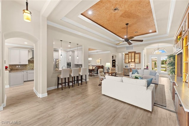 living room with a tray ceiling, ornamental molding, french doors, and light wood-type flooring