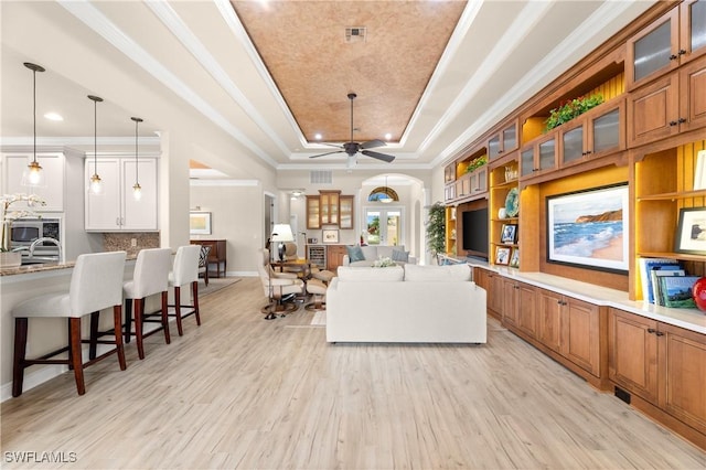 living room with ceiling fan, light hardwood / wood-style floors, a tray ceiling, and ornamental molding