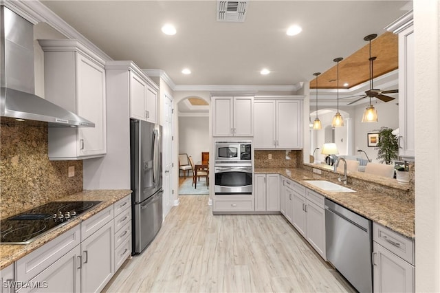 kitchen featuring white cabinetry, sink, decorative light fixtures, stainless steel appliances, and wall chimney exhaust hood