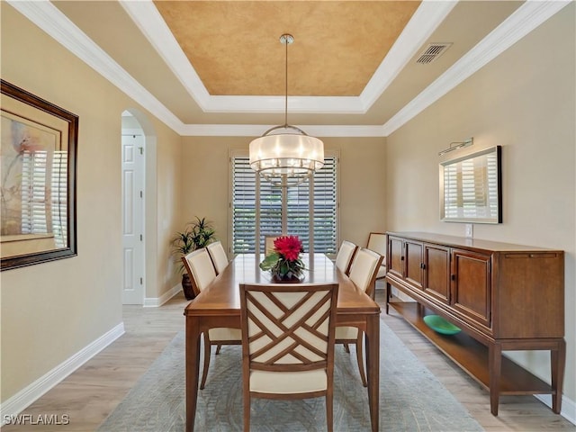 dining space with light hardwood / wood-style floors, a tray ceiling, and ornamental molding