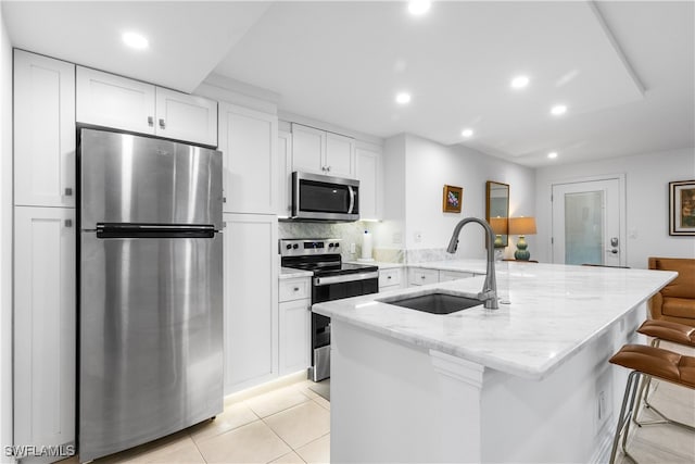 kitchen with sink, light stone countertops, appliances with stainless steel finishes, a breakfast bar area, and white cabinets