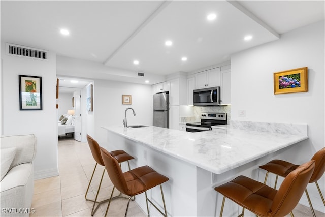 kitchen featuring kitchen peninsula, sink, white cabinetry, appliances with stainless steel finishes, and a breakfast bar area