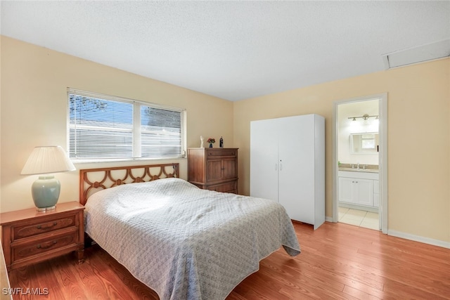 bedroom with ensuite bathroom, a textured ceiling, and light hardwood / wood-style flooring