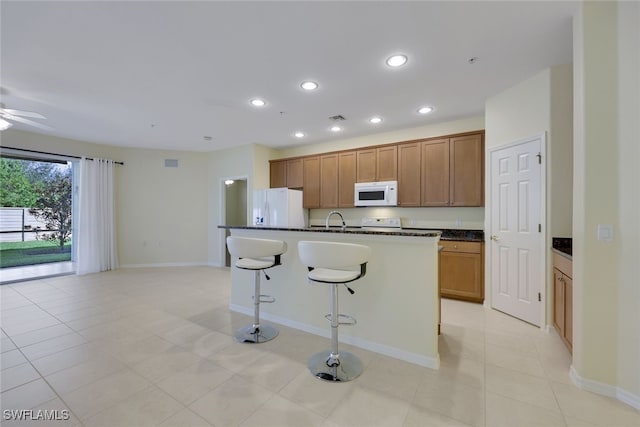 kitchen featuring light tile patterned floors, white appliances, a breakfast bar, ceiling fan, and a kitchen island with sink