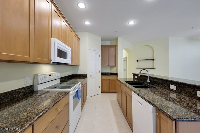 kitchen with sink, white appliances, dark stone counters, and light tile patterned flooring