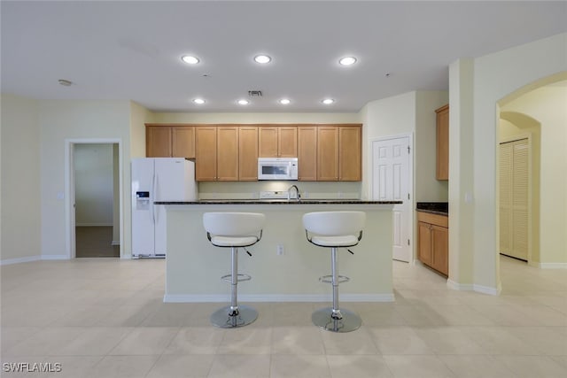 kitchen with white appliances, a kitchen bar, sink, and a center island with sink