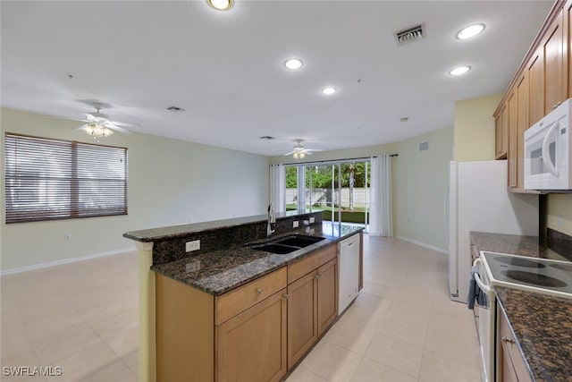 kitchen featuring sink, dark stone counters, a kitchen island with sink, ceiling fan, and white appliances