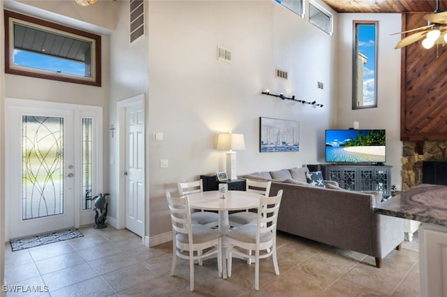 dining area featuring visible vents, light tile patterned floors, a fireplace, and a towering ceiling