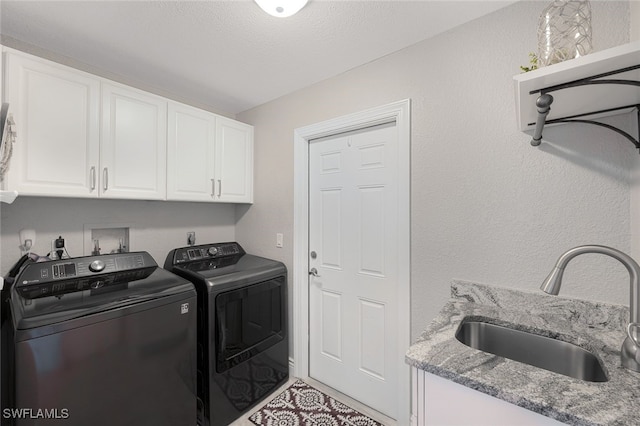 clothes washing area with cabinet space, a textured ceiling, washer and clothes dryer, and a sink