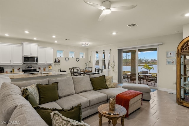 tiled living room with a water view, sink, and ceiling fan