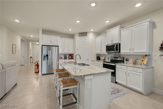 kitchen with white cabinetry, sink, stainless steel appliances, light stone countertops, and a center island with sink