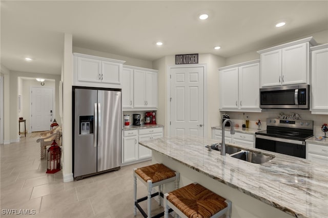 kitchen with sink, stainless steel appliances, light stone counters, white cabinets, and a kitchen bar