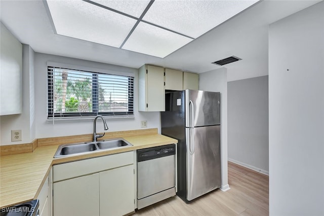 kitchen with appliances with stainless steel finishes, sink, cream cabinets, and light hardwood / wood-style floors