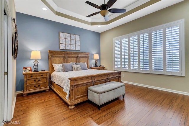 bedroom with ceiling fan, crown molding, a raised ceiling, and light wood-type flooring