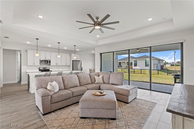 living room with ceiling fan, a raised ceiling, and sink