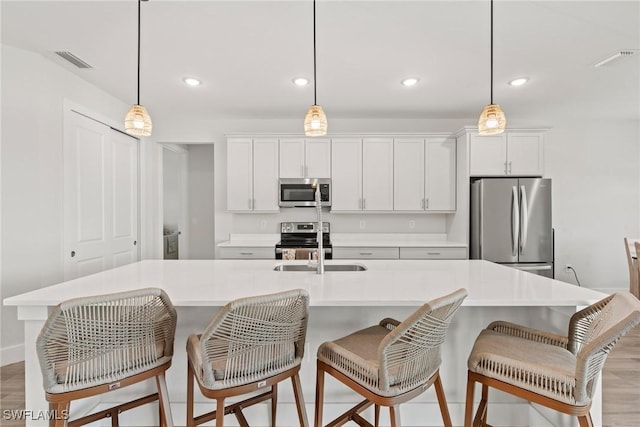 kitchen with hanging light fixtures, appliances with stainless steel finishes, white cabinets, and a large island with sink