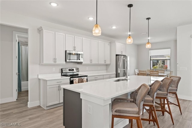 kitchen with an island with sink, appliances with stainless steel finishes, pendant lighting, and white cabinets