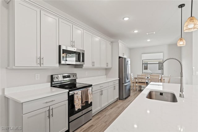 kitchen featuring appliances with stainless steel finishes, sink, white cabinets, and decorative light fixtures