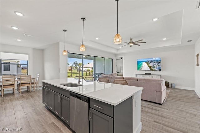 kitchen with a raised ceiling, appliances with stainless steel finishes, sink, and a kitchen island with sink