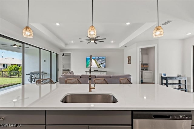 kitchen with pendant lighting, dishwasher, a kitchen island with sink, a tray ceiling, and washer / clothes dryer