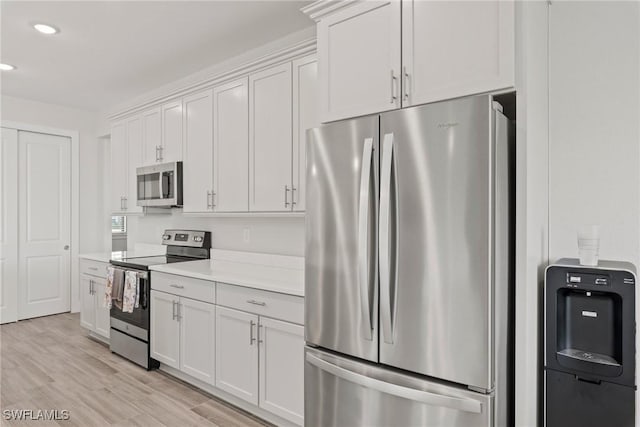 kitchen with appliances with stainless steel finishes, white cabinets, and light hardwood / wood-style flooring