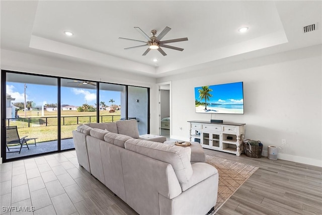 living room with light hardwood / wood-style flooring, a raised ceiling, and ceiling fan