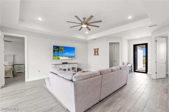 living room featuring a raised ceiling and ceiling fan