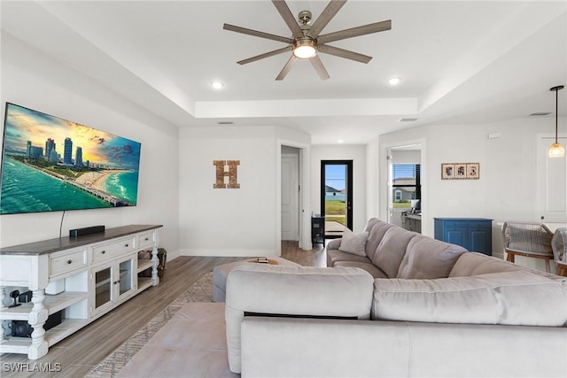 living room featuring ceiling fan, a raised ceiling, and light hardwood / wood-style floors