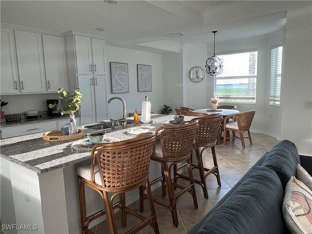 kitchen featuring pendant lighting, sink, a kitchen island with sink, light stone counters, and light tile patterned floors