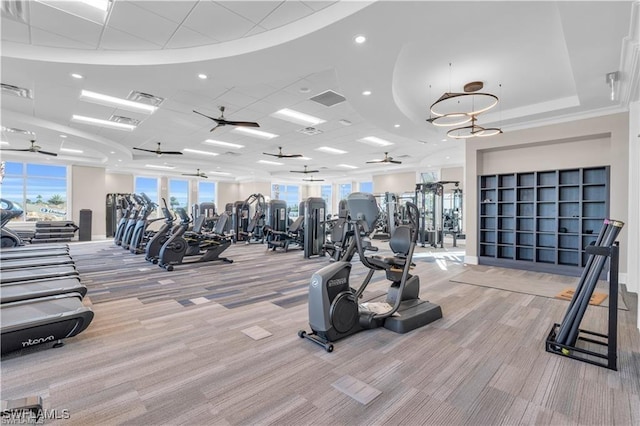 gym featuring ceiling fan, light colored carpet, and a raised ceiling