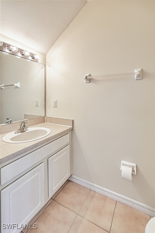 bathroom featuring vaulted ceiling, a textured ceiling, vanity, tile patterned flooring, and baseboards