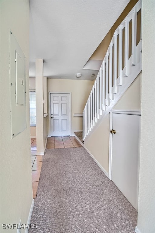 entrance foyer featuring light tile patterned floors, light carpet, baseboards, stairs, and electric panel