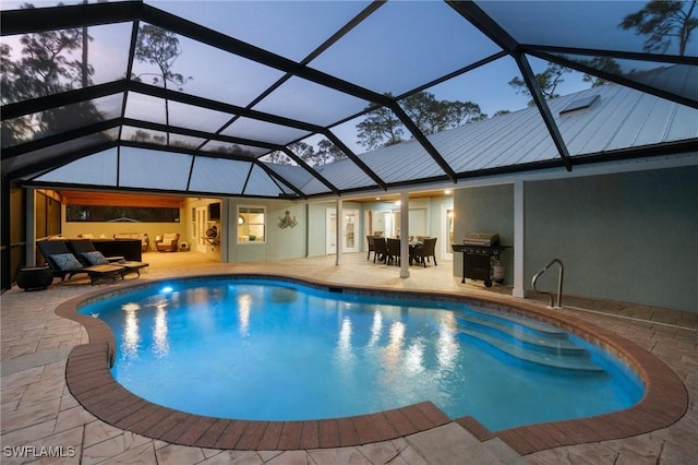 pool at dusk with area for grilling, a patio, and glass enclosure