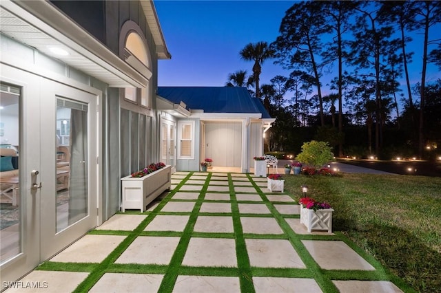 patio terrace at dusk featuring a lawn and french doors